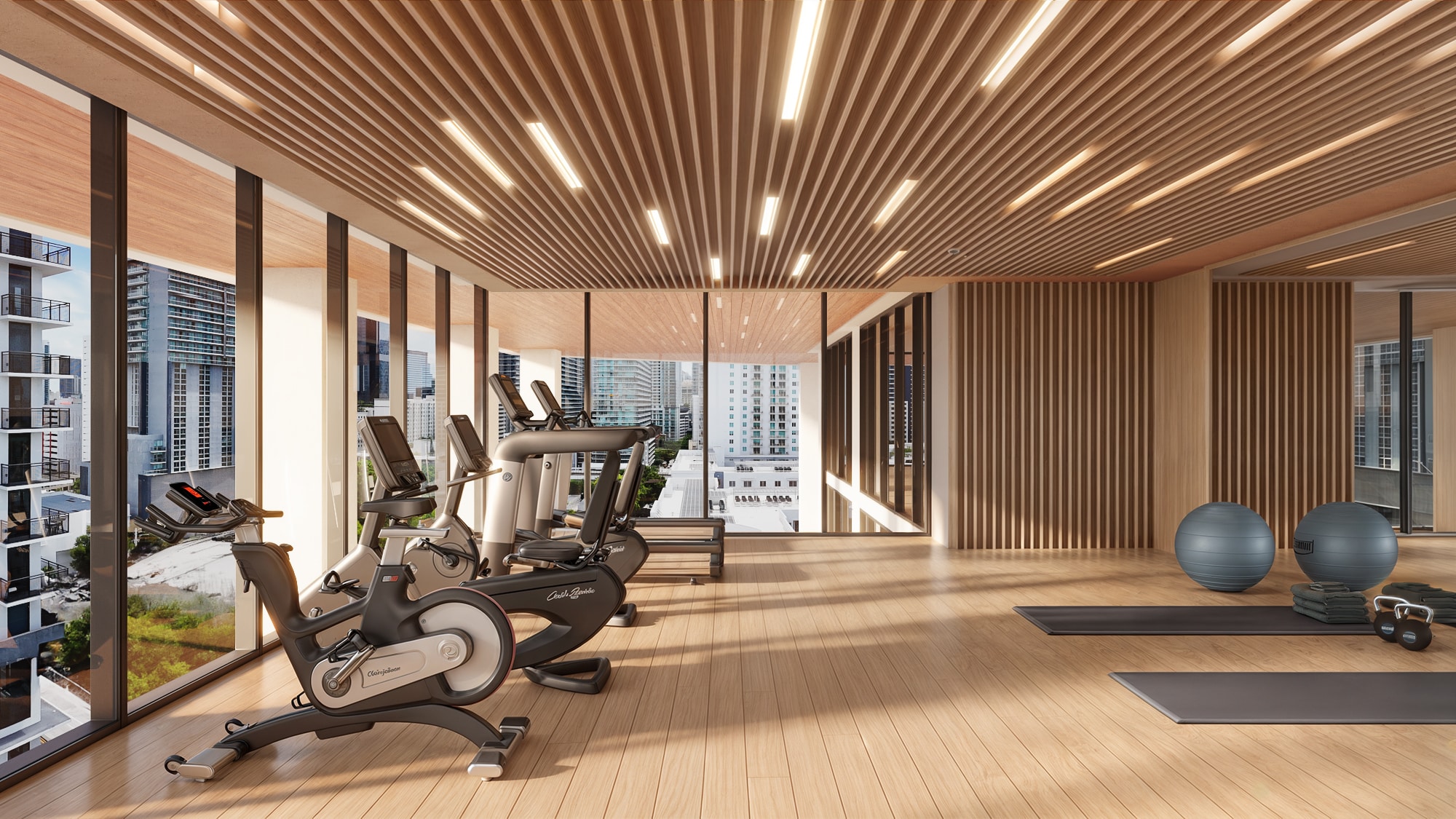 Gimnasio en Season One Brickell con máquinas de ejercicio, área de yoga y ventanales con vistas urbanas.